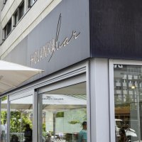 Außenansicht der Holanka Bar mit großen Sonnenschirmen. Menschen sitzen und stehen im Außenbereich. Moderne Gebäude im Hintergrund., © SMG, Sarah Schmid Außenansicht der Holanka Bar mit großen Sonnenschirmen. Menschen sitzen und stehen im Außenbereich. Moderne Gebäude im Hintergrund., © SMG, Sarah Schmid