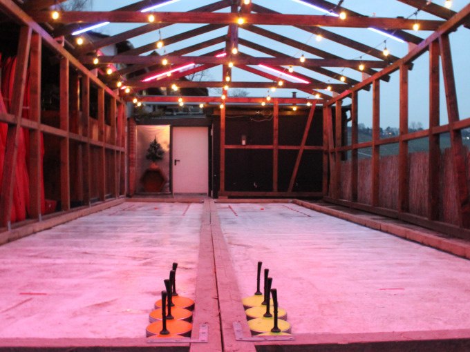 A covered curling rink with colorful lights and curling sticks, surrounded by a wooden structure., &copy; Cool-Tours StattReisen