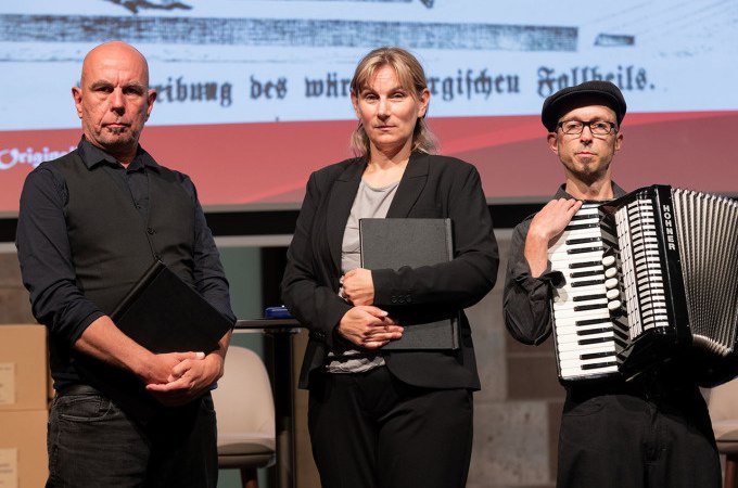 Drei Personen auf einer Bühne, zwei mit Büchern, eine mit Akkordeon. Hintergrund zeigt historischen Text., © Landesmuseum Württemberg Drei Personen auf einer Bühne, zwei mit Büchern, eine mit Akkordeon. Hintergrund zeigt historischen Text., © Landesmuseum Württemberg