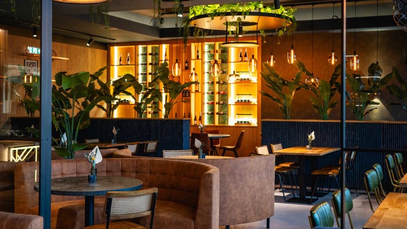 A stylish dining room with modern furniture, plants and warm lighting. Wooden tables and leather seats create an inviting atmosphere., © SatzDrei