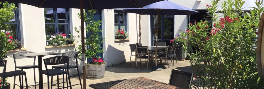 Sunny terrace of a winery with wooden tables, chairs and blue parasols. Flowers and plants adorn the outdoor area., © Weingut Wöhrwag