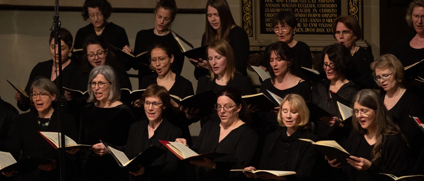 Women's choir in black clothing singing in a church, holding sheet music. Background with decorative writing., © www.hassfoto.de