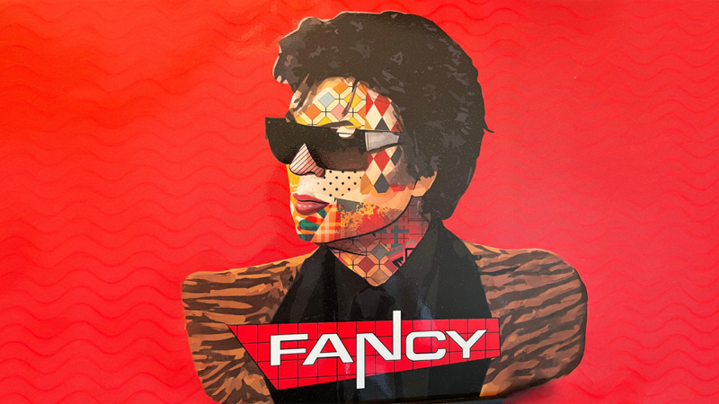Stilisierte Illustration eines Mannes mit Sonnenbrille vor rotem Hintergrund. Der Schriftzug 'FANCY' ist prominent platziert., &copy; links im Bild