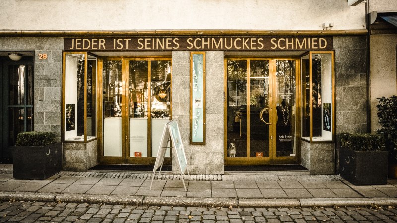Ein Schmuckgeschäft mit der Aufschrift 'Jeder ist seines Schmuckes Schmied' über dem Eingang. Die Fassade ist aus Stein, mit großen Fenstern und einer Holztür., © Goldmond Ein Schmuckgeschäft mit der Aufschrift 'Jeder ist seines Schmuckes Schmied' über dem Eingang. Die Fassade ist aus Stein, mit großen Fenstern und einer Holztür., © Goldmond