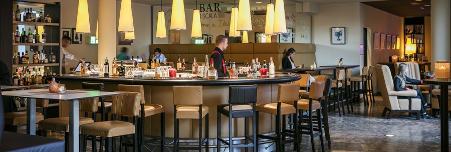 Modern bar with round counter, hanging lamps and seating areas in the Arcotel Camino. People sit and enjoy the atmosphere., &copy; &copy; Harald Eisenberger
