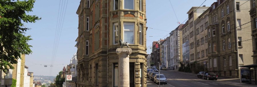 The Loriot memorial on Eugensplatz in Stuttgart shows a column with a sculpture on it. Historical buildings and a street can be seen in the background., &copy; Stuttgart-Marketing GmbH