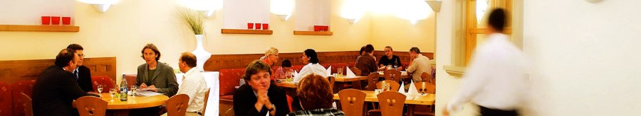 Gemütliches Restaurant mit Holzmöbeln, mehreren Gästen an Tischen und einem Kellner in Bewegung. Warme Beleuchtung und dekorative Elemente an den Wänden., © SMG