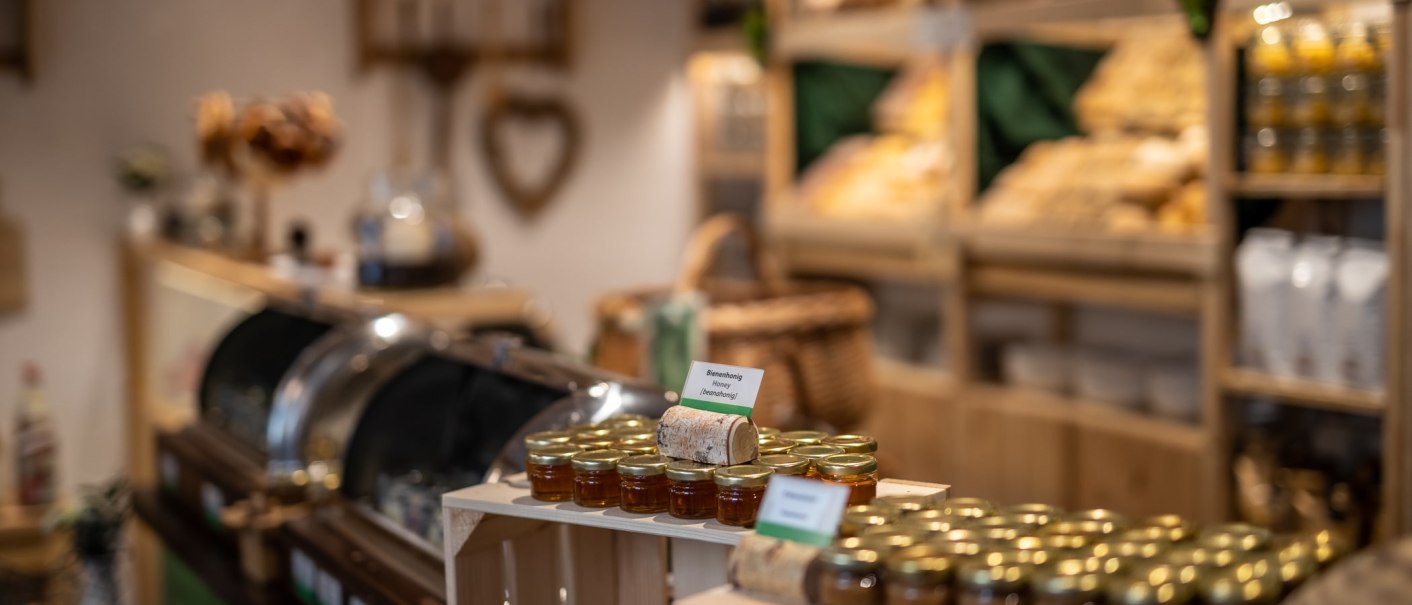A cozy store with honey jars on wooden shelves and bread baskets in the background. The room looks inviting and rustic., &copy; TOMAS