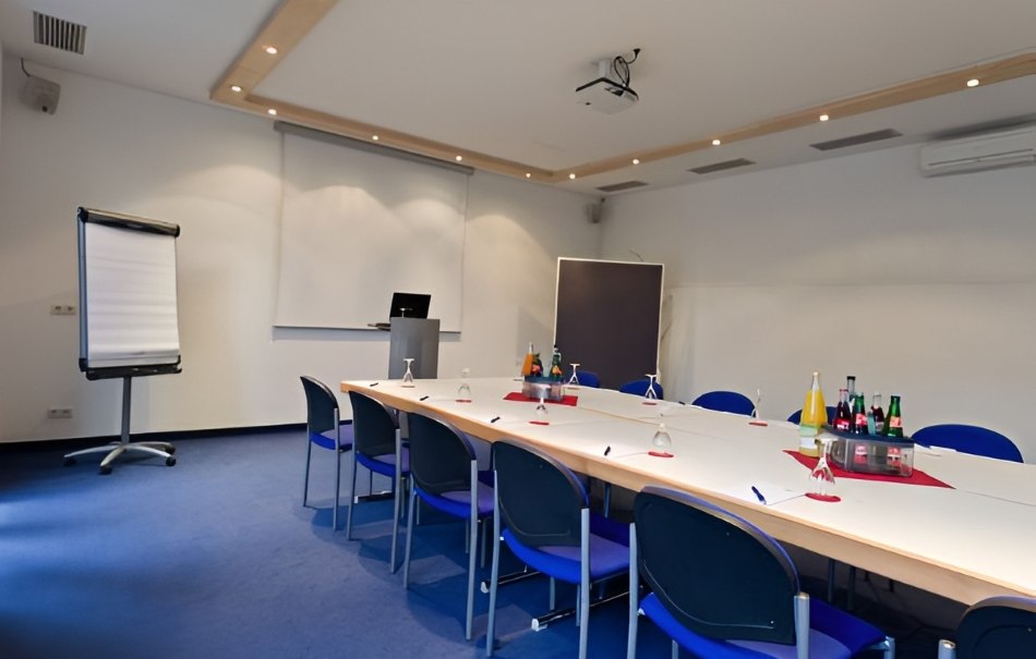Modern conference room with a large table, blue chairs, flipchart and drinks. A projector on the ceiling and a screen on the wall., © Hotel Neuwirtshaus Modern conference room with a large table, blue chairs, flipchart and drinks. A projector on the ceiling and a screen on the wall., © Hotel Neuwirtshaus