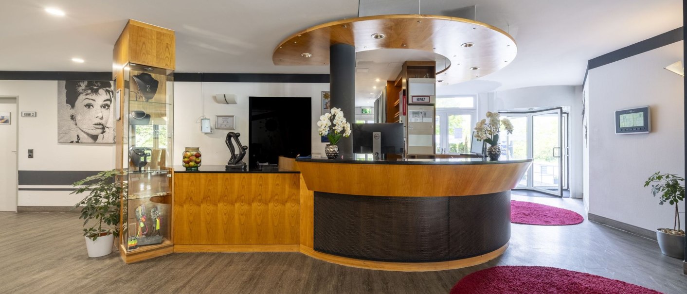 Modern reception area with wooden counter, orchids and a picture on the wall. Red carpets and glass doors in the background., © Plaza INN Stuttgart-Filderstadt Modern reception area with wooden counter, orchids and a picture on the wall. Red carpets and glass doors in the background., © Plaza INN Stuttgart-Filderstadt