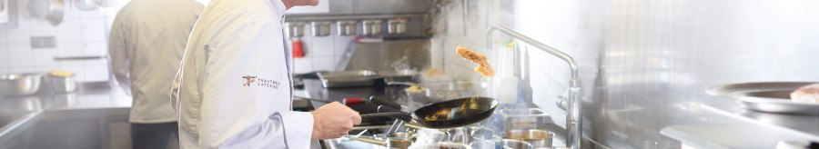A chef in a white uniform fries meat in a pan in a professional kitchen. Another chef can be seen in the background., © SMG, Jean-Claude Winkler