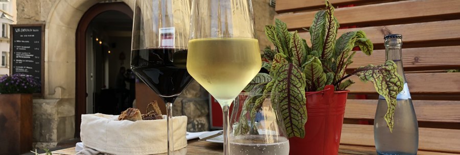 A table with a glass of red and white wine, bread, a small dish and a plant in front of the 'Speisekammer West' restaurant., &copy; Speisekammer West