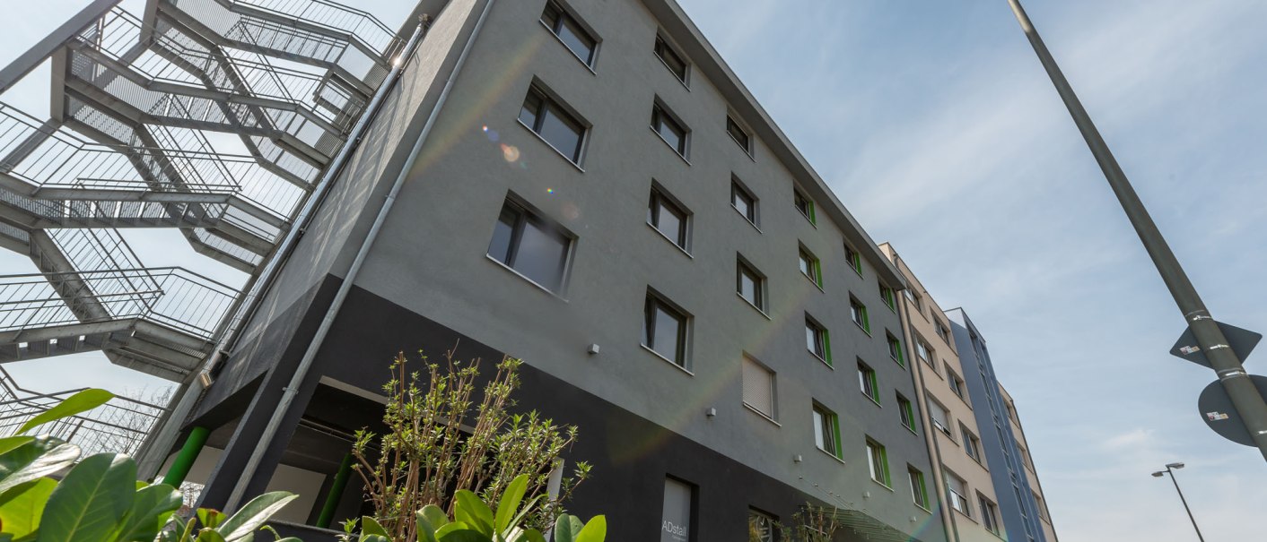 Modern hotel building with fire escape, surrounded by green plants, under a blue sky., &copy; a2 HOTELS