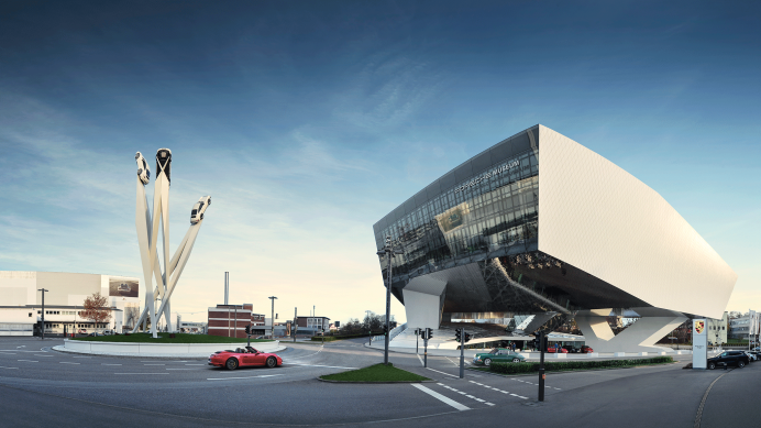Das Porsche Museum in Stuttgart mit futuristischer Architektur und einer Skulptur von drei Autos auf hohen Säulen vor blauem Himmel., © Porsche AG