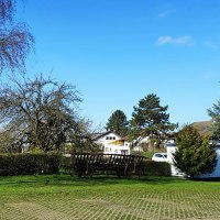 Ein Wohnmobilstellplatz mit Bäumen und einem Parkplatzschild. Im Hintergrund sind Häuser und ein blauer Himmel zu sehen., © Dieter Schurr, Gasthaus Hirsch