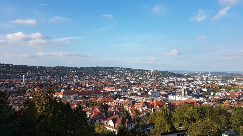 Panoramablick auf eine Stadt mit roten D&auml;chern, umgeben von gr&uuml;nen H&uuml;geln und blauem Himmel., &copy; SMG