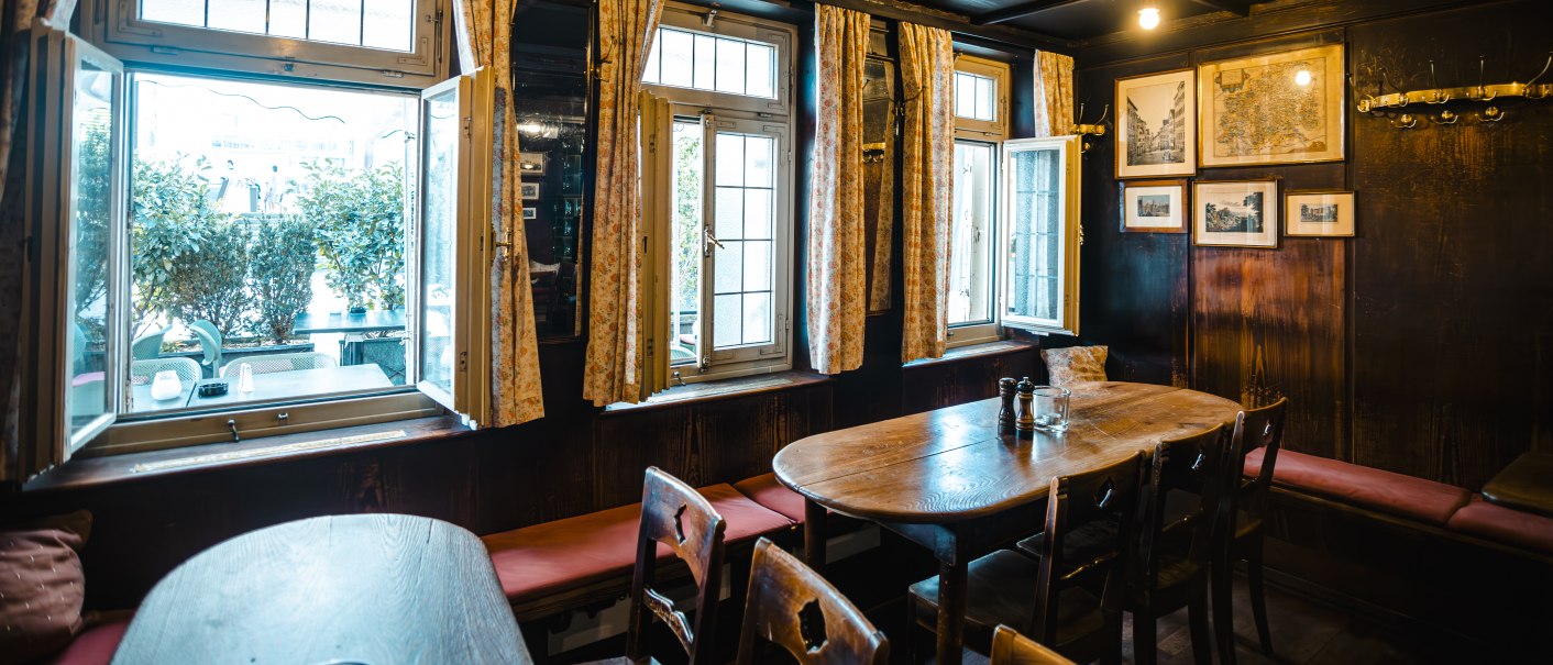 Gemütliche Weinstube mit Holztischen, Stühlen und offenen Fenstern. Die Wände sind mit Bildern dekoriert, und es gibt eine warme Beleuchtung., © SMG Stuttgart Marketing GmbH - Sarah Schmid Gemütliche Weinstube mit Holztischen, Stühlen und offenen Fenstern. Die Wände sind mit Bildern dekoriert, und es gibt eine warme Beleuchtung., © SMG Stuttgart Marketing GmbH - Sarah Schmid