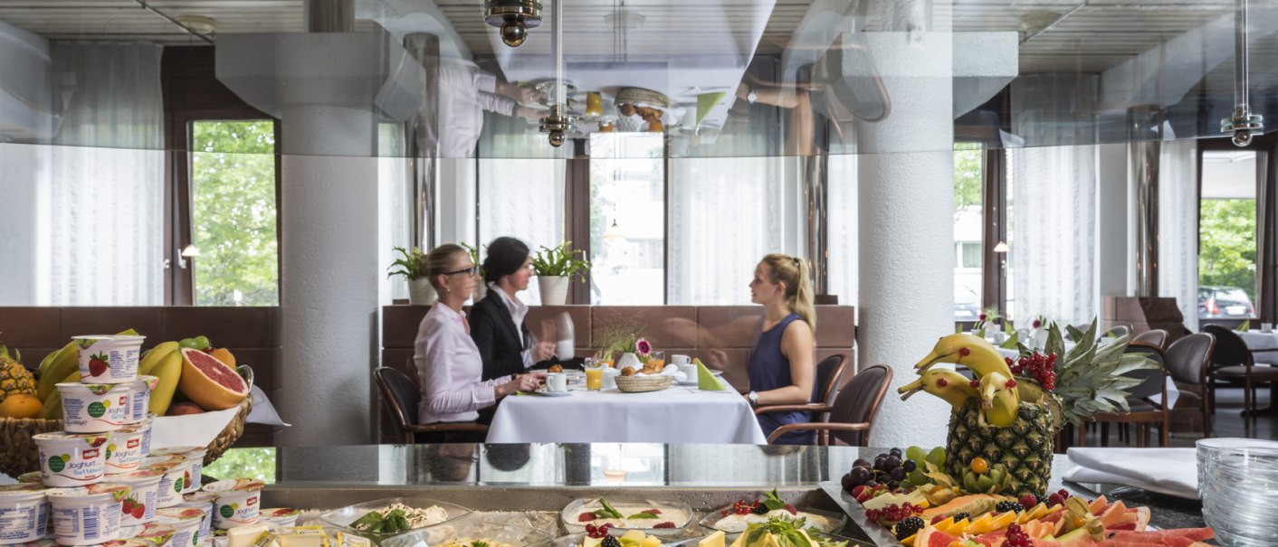 A hearty breakfast buffet with yogurt, fruit, and cheese. In the background, three people are sitting at a table and chatting., &copy; Hotel Berlin aZIS Hotel BetriebsGmbH