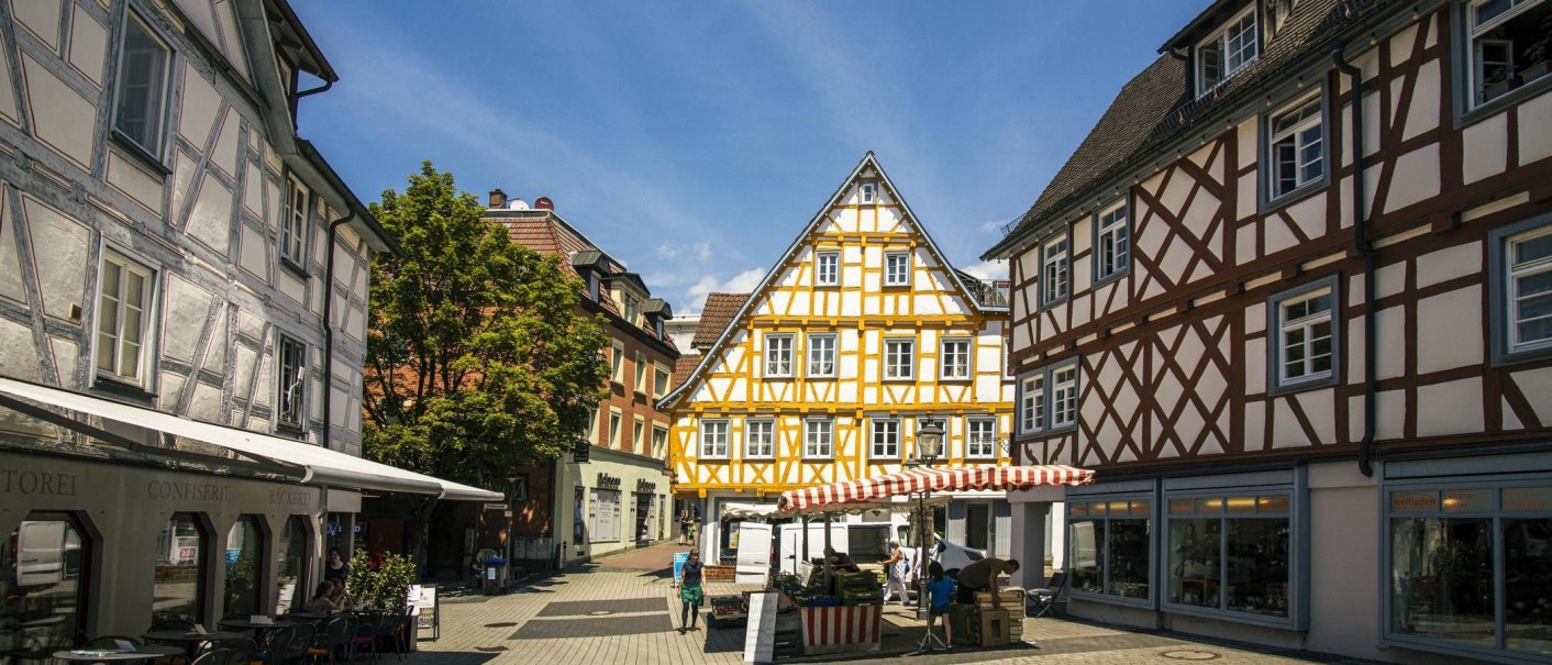 Half-timbered houses in the old town of Backnang, surrounded by market stalls and passers-by in sunny weather., © Stuttgart-Marketing GmbH, Sarah Schmid