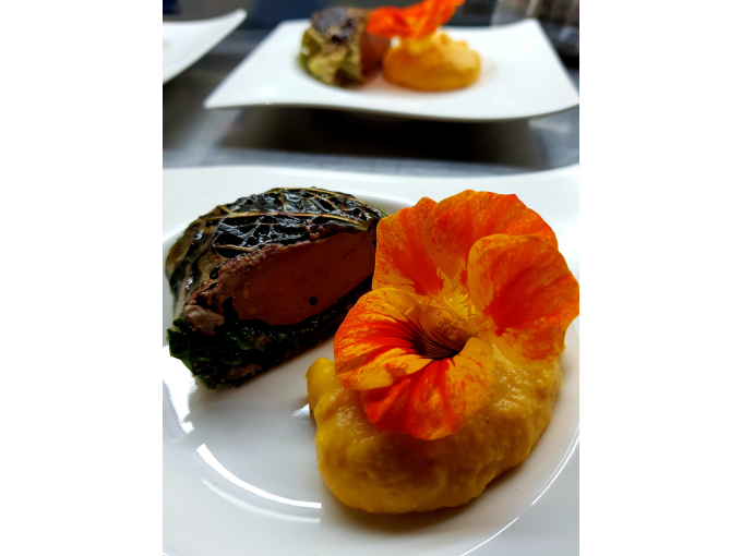 Ein kunstvoll angerichtetes Gericht mit Fleisch, Kürbispüree und einer orangefarbenen essbaren Blume auf einem weißen Teller., © Kultweine-Kochwelten-Kunstücke - Kochschule Sonja Lenz Ein kunstvoll angerichtetes Gericht mit Fleisch, Kürbispüree und einer orangefarbenen essbaren Blume auf einem weißen Teller., © Kultweine-Kochwelten-Kunstücke - Kochschule Sonja Lenz