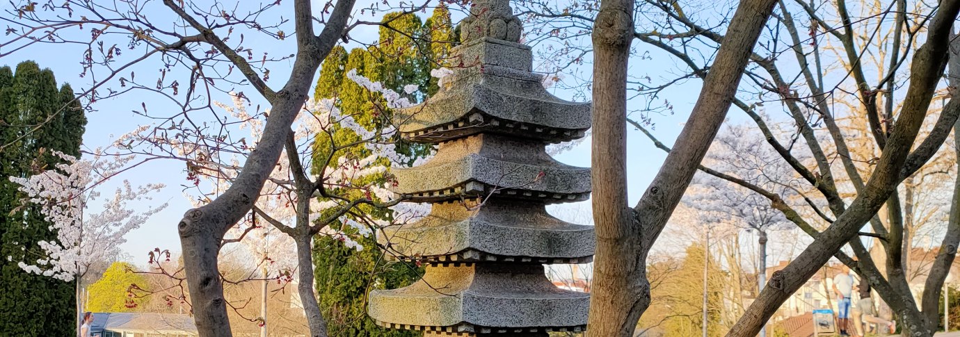Eine Steinpagode steht in einem Garten, umgeben von bl&uuml;henden B&auml;umen und gr&uuml;nem Rasen. Der Himmel ist klar und blau., &copy; SMG