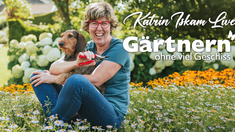 Eine Frau mit roter Brille sitzt lachend auf einer Blumenwiese, h&auml;lt eine Gartenschere und einen Hund im Arm. Im Hintergrund bl&uuml;hende Hortensien., &copy; links im Bild