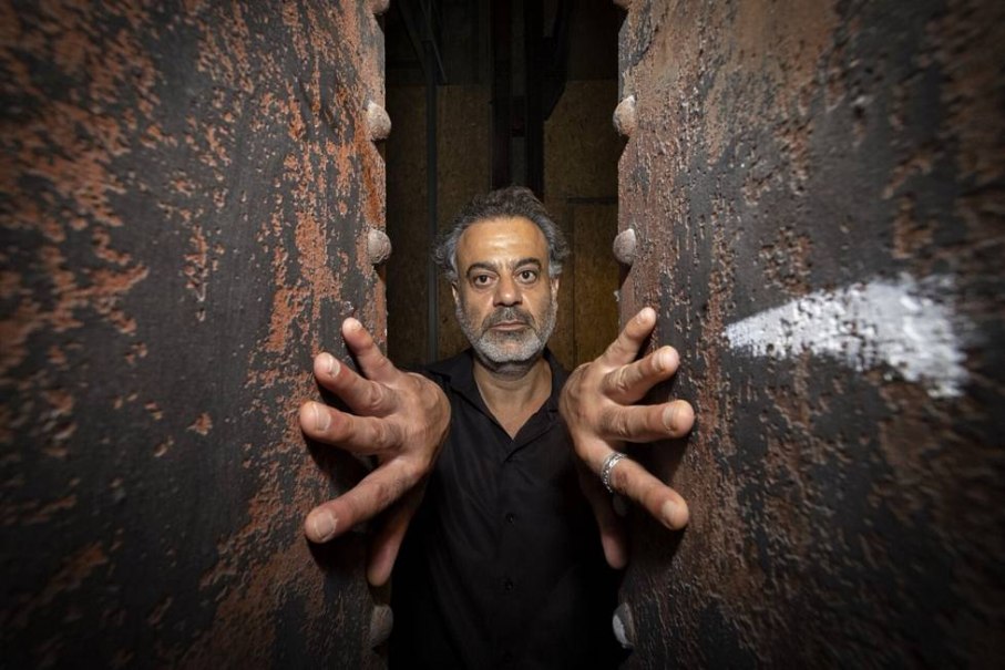 Ein Mann steht mit ausgebreiteten Armen zwischen zwei rostigen Metallplatten und blickt ernst in die Kamera., &copy; privat