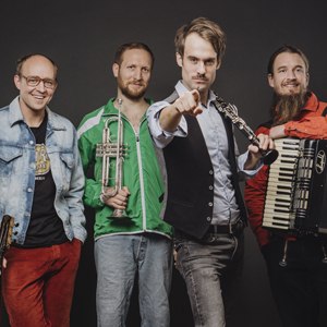 Vier Männer mit Musikinstrumenten posieren vor einem dunklen Hintergrund. Einer zeigt mit dem Finger nach vorne, die anderen halten Trompete und Akkordeon., © Renitenztheater Stuttgart e.V.