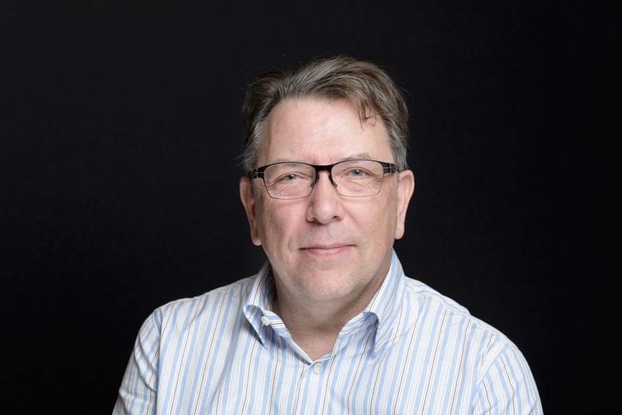 Ein Mann mit Brille und gestreiftem Hemd l&auml;chelt leicht in die Kamera. Der Hintergrund ist schwarz, was den Fokus auf das Gesicht lenkt., &copy; Foto: Gerrit Mumme