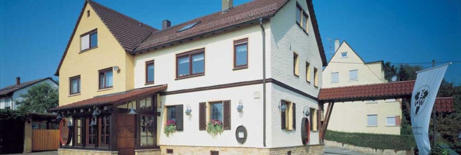 Two-storey building with a yellow and white fa&ccedil;ade and red roof tiles. A VdW banner stands in front of it. Clear blue sky in the background., &copy; Weinstube J&auml;gerhof