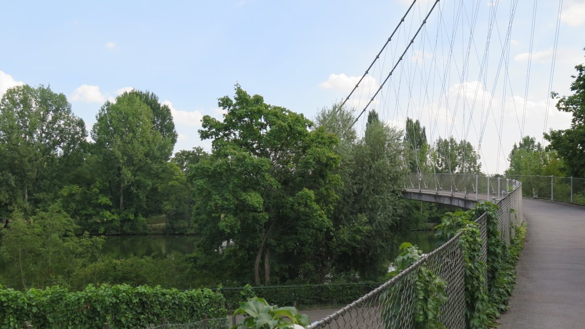 Der Max-Eyth-Steg ist eine Fußgängerbrücke, die über einen Fluss führt, umgeben von üppigem Grün und Bäumen. Der Himmel ist leicht bewölkt., © Stuttgart-Marketing GmbH Der Max-Eyth-Steg ist eine Fußgängerbrücke, die über einen Fluss führt, umgeben von üppigem Grün und Bäumen. Der Himmel ist leicht bewölkt., © Stuttgart-Marketing GmbH