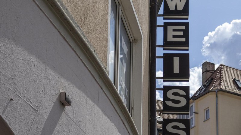 A sign saying 'WHITE' hangs on a building. The sky is blue with a few clouds. Roofs can be seen in the background., &copy; SMG, Sarah Schmid