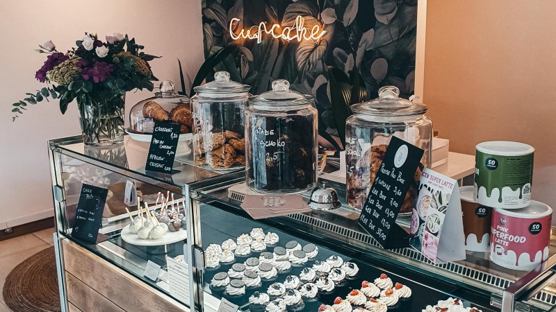 Ein Café mit einer Glasvitrine voller Cupcakes und Kekse. Ein Neon-Schild mit 'Cupcake' leuchtet im Hintergrund. Blumen schmücken den Tresen., © Cupcakes & Bagels, Stuttgart Ein Café mit einer Glasvitrine voller Cupcakes und Kekse. Ein Neon-Schild mit 'Cupcake' leuchtet im Hintergrund. Blumen schmücken den Tresen., © Cupcakes & Bagels, Stuttgart