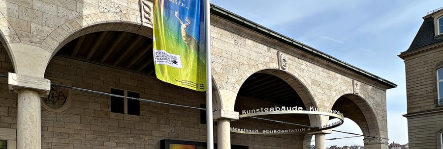 Eingang der Staatsgalerie mit bunten Plakaten zur Ausstellung von Katharina Grosse. Ein großes Banner hängt an einem Mast., © Staatsgalerie
