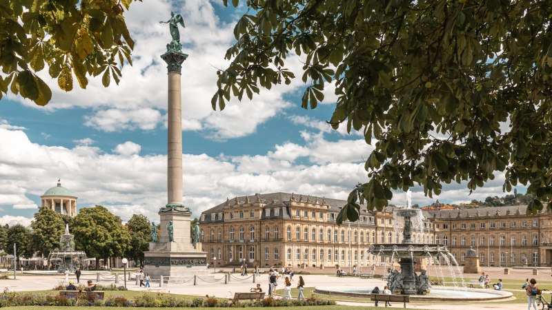 Der Schlossplatz in Stuttgart mit der Jubiläumssäule und dem Neuen Schloss im Hintergrund. Menschen spazieren und entspannen im sonnigen Park., © SMG, Sarah Schmid Der Schlossplatz in Stuttgart mit der Jubiläumssäule und dem Neuen Schloss im Hintergrund. Menschen spazieren und entspannen im sonnigen Park., © SMG, Sarah Schmid