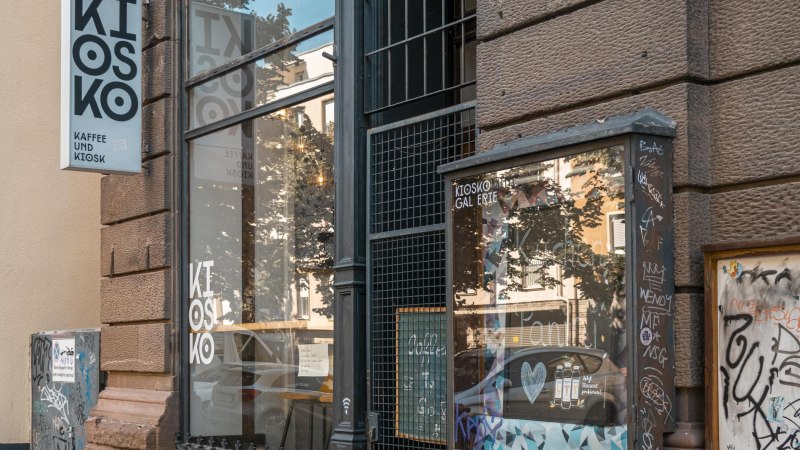Ein Kiosk mit der Aufschrift 'Kiosko Kaffee und Kiosk'. Die Fassade ist mit Graffiti bedeckt, und das Schaufenster spiegelt die Umgebung wider., © SMG, Sarah Schmid Ein Kiosk mit der Aufschrift 'Kiosko Kaffee und Kiosk'. Die Fassade ist mit Graffiti bedeckt, und das Schaufenster spiegelt die Umgebung wider., © SMG, Sarah Schmid