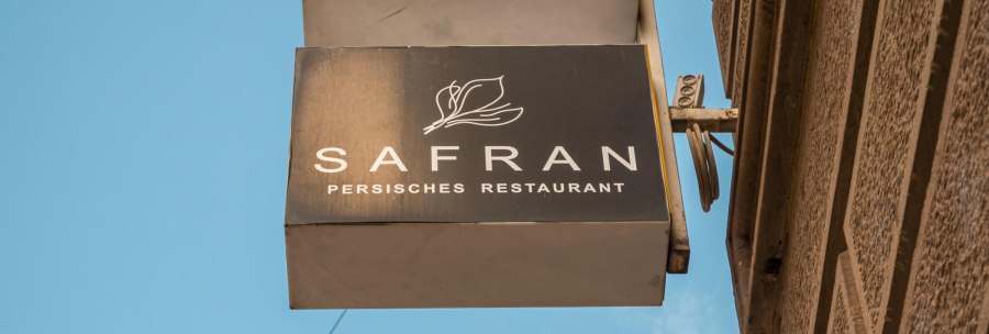 Schild eines persischen Restaurants namens Safran an einer Hauswand, vor blauem Himmel., © SMG, Sarah Schmid