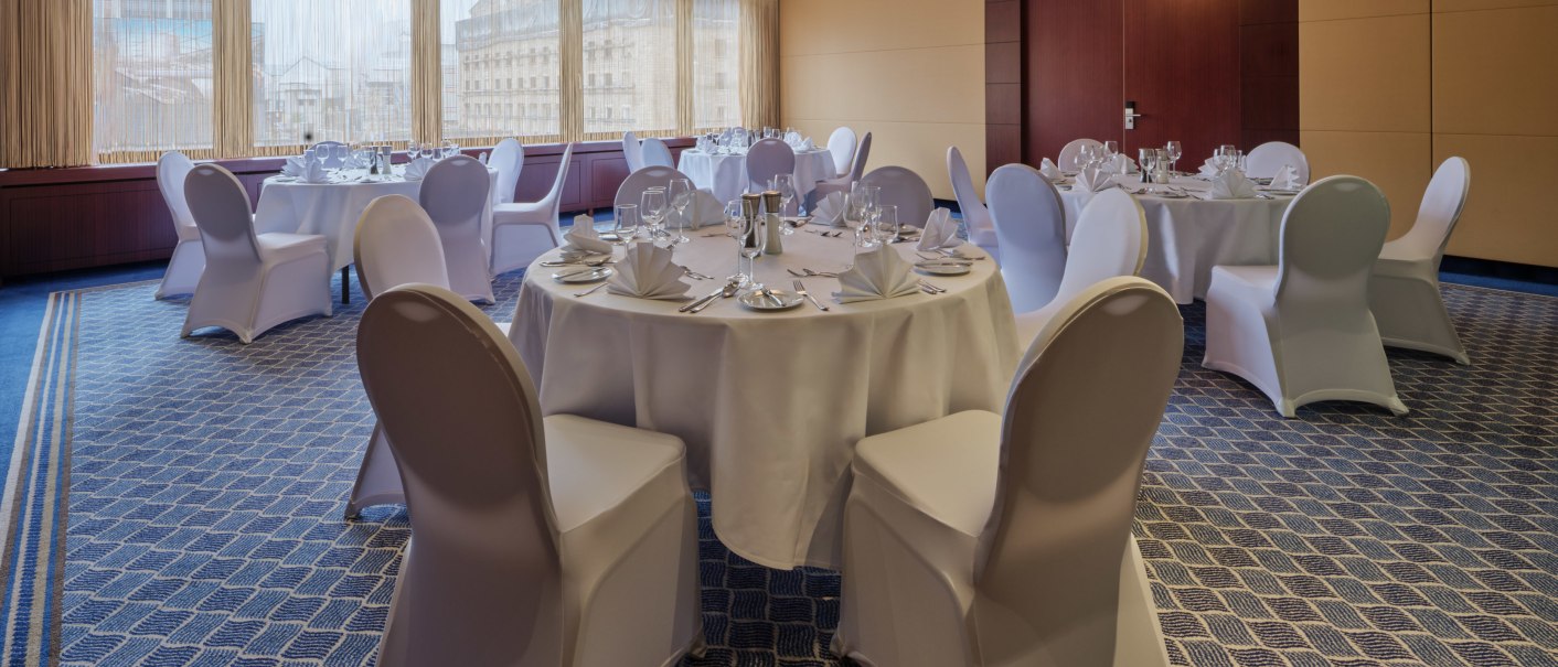 Elegant banquet hall with round, festively laid tables and white chair covers, large chandelier on the ceiling., © Steigenberger Graf Zeppelin