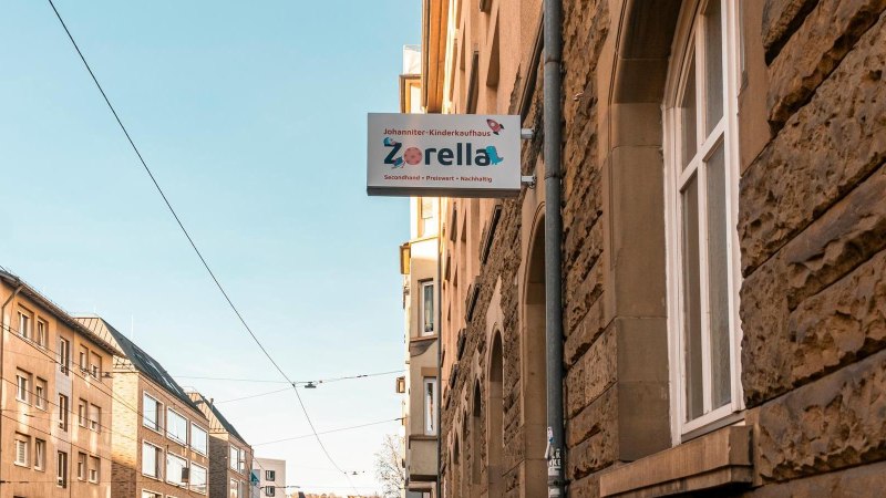Schild des Johanniter-Kinderkaufhauses Zorella an einer Hauswand in einer sonnigen Straße mit Altbauten., © Stuttgart-Marketing GmbH, Sarah Schmid Schild des Johanniter-Kinderkaufhauses Zorella an einer Hauswand in einer sonnigen Straße mit Altbauten., © Stuttgart-Marketing GmbH, Sarah Schmid