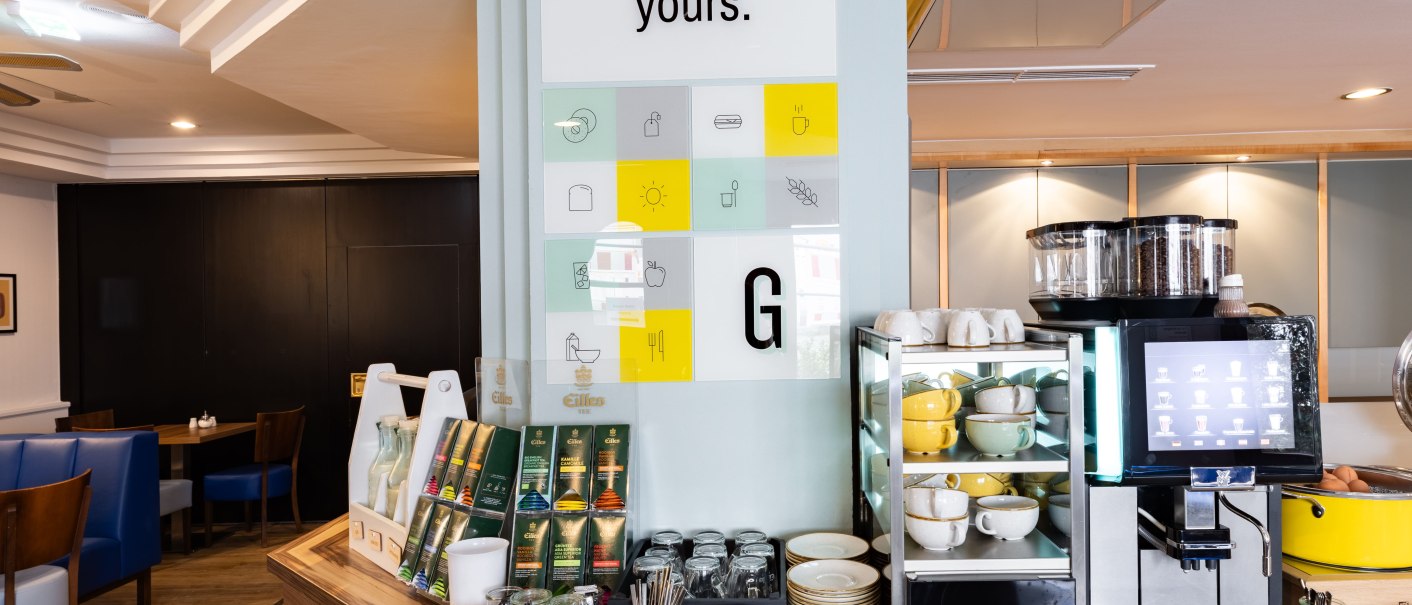 A breakfast room with a coffee maker, cups, plates, and a selection of teas. A sign that reads "Make it yours" is visible., &copy; Novum  Hospitality