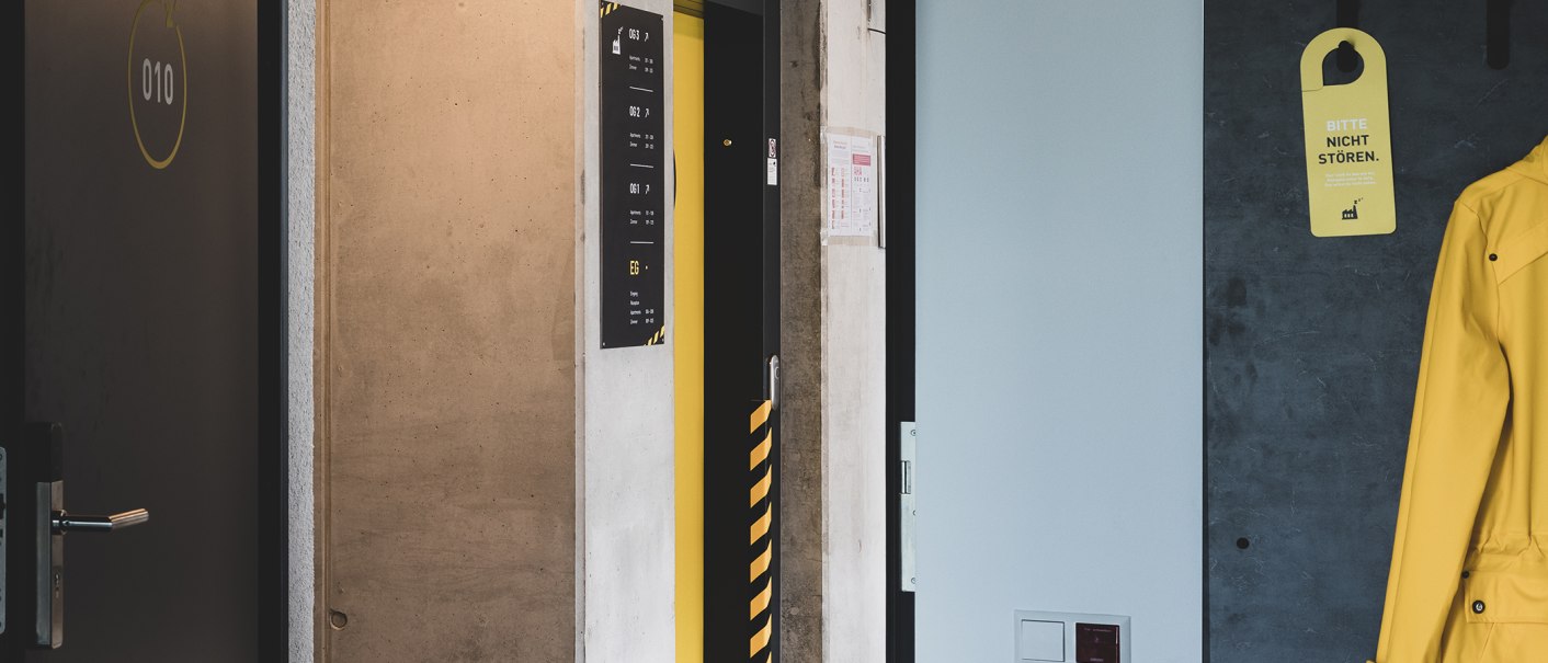 Flur mit einer gelben Jacke an der Wand, einem Türschild 'Bitte nicht stören' und einer Tür mit der Nummer 010., © Das Schlafwerk - DQuadrat Living GmbH