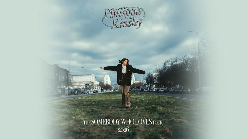 Eine Person steht mit ausgebreiteten Armen auf einem Grünstreifen in einer städtischen Umgebung. Der Himmel ist bewölkt, und im Hintergrund sind Gebäude und Bäume zu sehen., © links im Bild Eine Person steht mit ausgebreiteten Armen auf einem Grünstreifen in einer städtischen Umgebung. Der Himmel ist bewölkt, und im Hintergrund sind Gebäude und Bäume zu sehen., © links im Bild