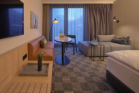 Modern hotel room with sofa, table, bed and large windows. Subtle lighting and stylish decoration create a cozy atmosphere., &copy; Adina Apartment Hotel Stuttgart