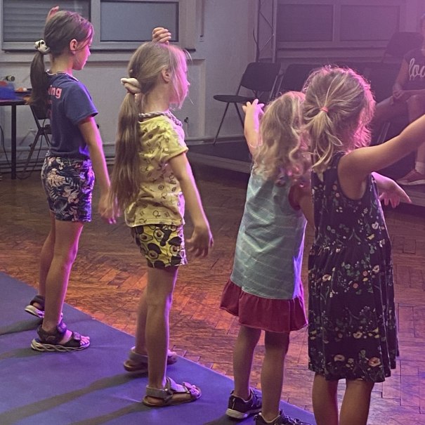 Fünf Kinder tanzen in einem Raum mit Holzboden. Sie tragen Sommerkleidung und scheinen eine Choreografie zu üben., © Tathea - Lena Oschowitzer Fünf Kinder tanzen in einem Raum mit Holzboden. Sie tragen Sommerkleidung und scheinen eine Choreografie zu üben., © Tathea - Lena Oschowitzer