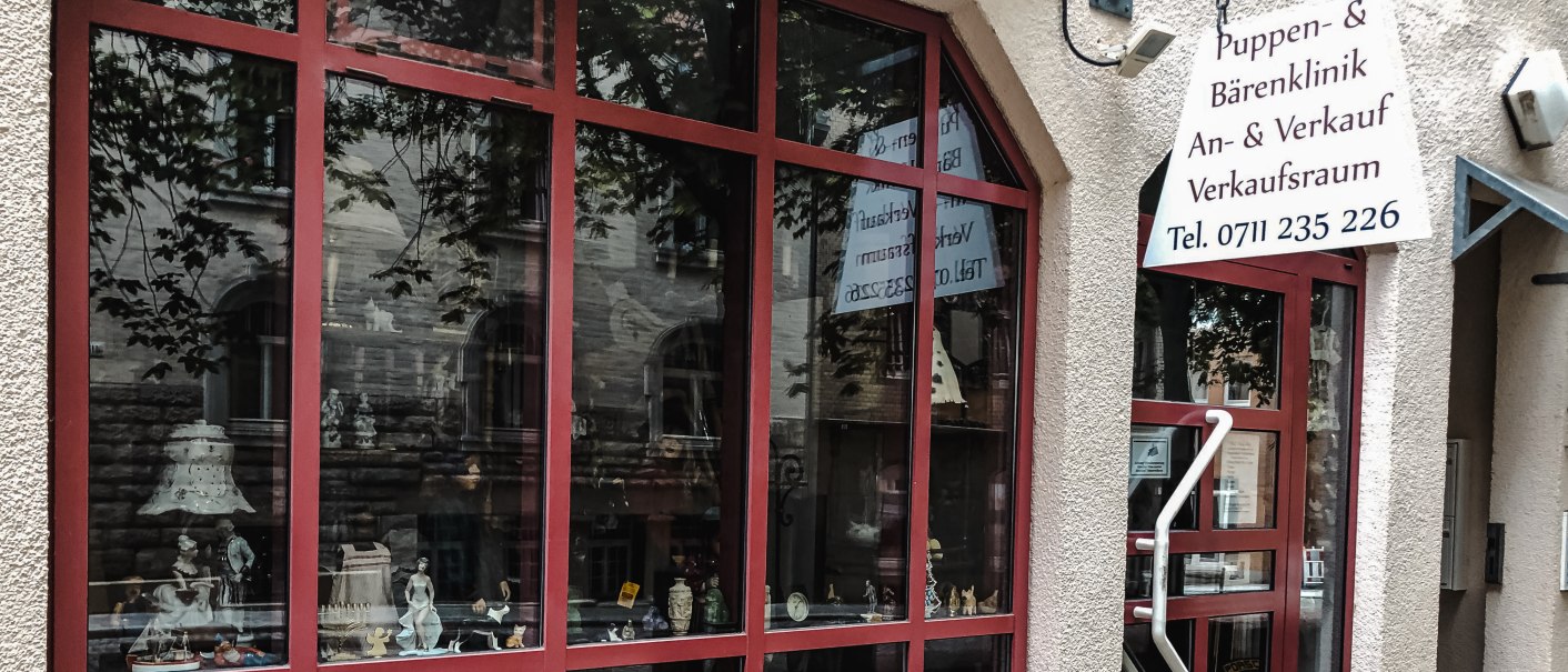 Schaufenster einer Puppen- und Bärenklinik mit verschiedenen Dekorationen. Ein Schild mit der Telefonnummer hängt über der Tür., © Puppen- und Bärenklinik