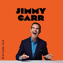 Ein Mann in einem Anzug lacht vor einem orangefarbenen Hintergrund. Oben steht der Name 'Jimmy Carr'., © links im Bild Ein Mann in einem Anzug lacht vor einem orangefarbenen Hintergrund. Oben steht der Name 'Jimmy Carr'., © links im Bild