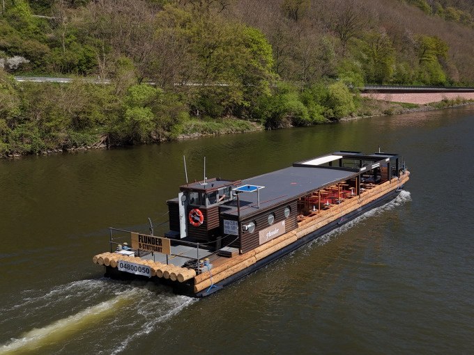 Das Flussschiff Flunder fährt auf einem Fluss, umgeben von grüner Landschaft. An Bord sind Sitzplätze für Gäste., © Cool-Tours StattReisen Das Flussschiff Flunder fährt auf einem Fluss, umgeben von grüner Landschaft. An Bord sind Sitzplätze für Gäste., © Cool-Tours StattReisen