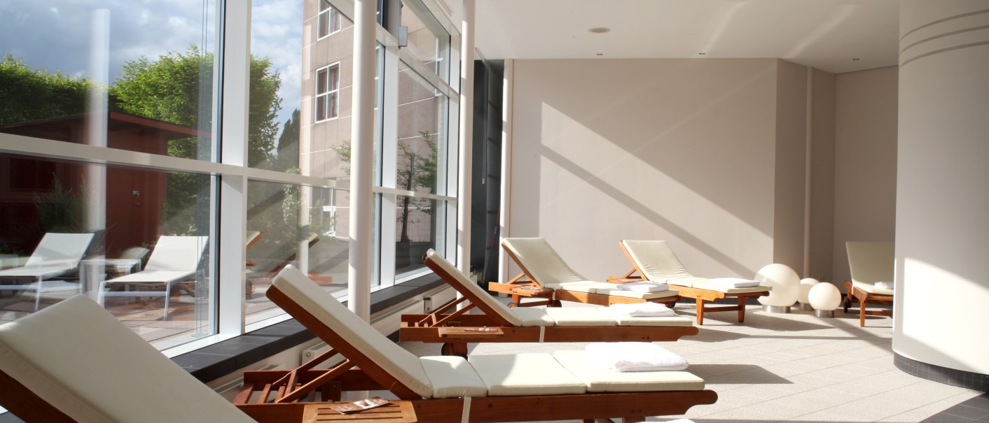 Heller Wellnessbereich mit Liegestühlen und großen Fenstern, die viel Tageslicht hereinlassen. Handtücher liegen auf den Stühlen bereit., © Pullman Stuttgart Fontana