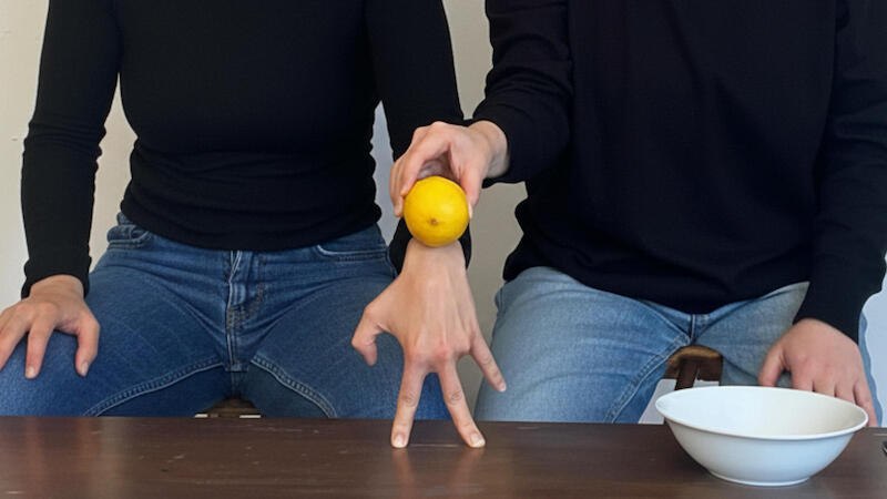 Zwei Personen in schwarzen Oberteilen und Jeans sitzen an einem Tisch. Eine Person h&auml;lt eine Zitrone auf der Hand der anderen. Eine wei&szlig;e Sch&uuml;ssel steht daneben., &copy; FITZ Das Theater animierter Formen