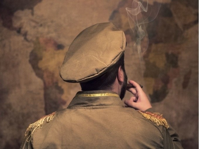 Person in Milit&auml;runiform mit M&uuml;tze raucht vor einer Weltkarte. Der Hintergrund ist unscharf, der Rauch ist sichtbar., &copy; ExitGames Stuttgart